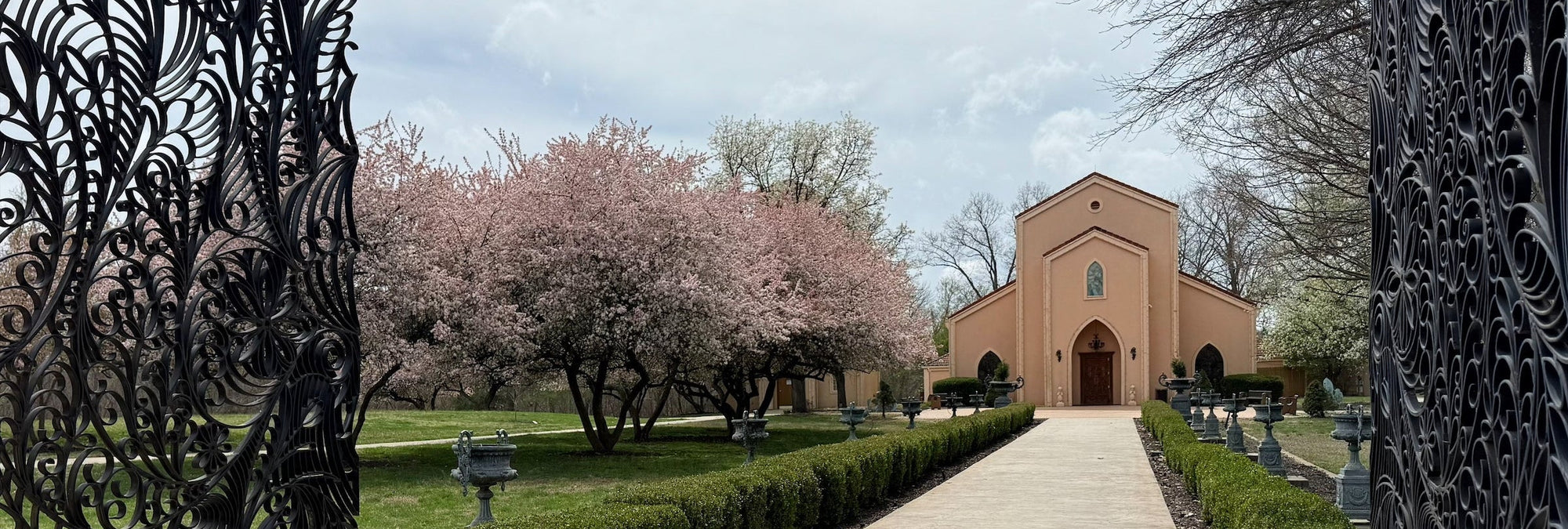 Beautiful gates opening to a scene of the Precious Moments Chapel surrounded by flowering trees